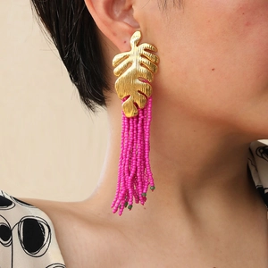 Detail of leaf-shaped metal earrings with bright pink bead tassels in bohemian style