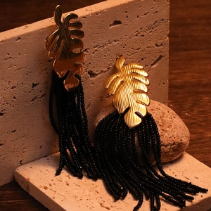 Detail of gold hollow leaf earrings with black seed bead tassels on stone display