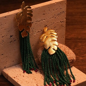 Detailed shot of tropical monstera leaf earrings with green beaded fringe on stones
