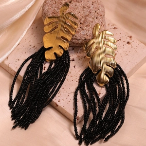Detailed shot of golden monstera leaf earrings with long black seed bead tassels