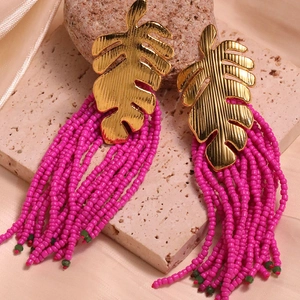 Detailed shot of golden leaf earrings with vibrant magenta bead tassels on marble background