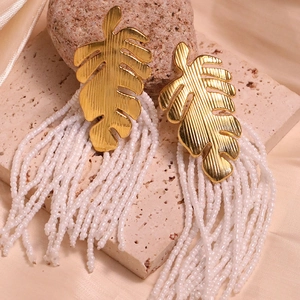Macro shot of gold monstera leaf alloy stud with long white seed bead tassel earrings