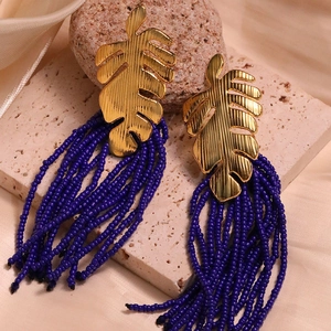 Macro shot of gold monstera leaf stud earring with deep purple beaded tassel fringe details