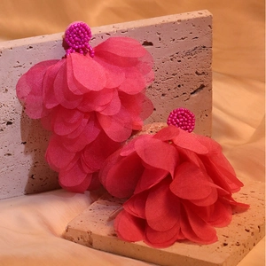 Close-up of handmade fuchsia fabric tassel earrings with beaded disks on travertine