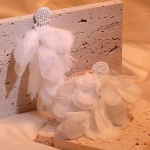 Detailed view of handmade white fabric petal tassel earrings on a natural stone background