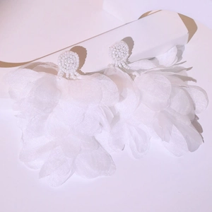 Close-up of handmade white fabric flower tassel earrings with woven bead details