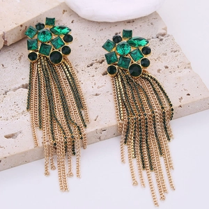 Macro detail of long tassel earrings with green crystals on a beige stone display