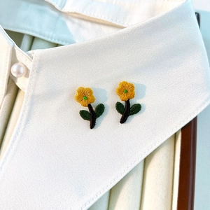 Detailed close-up of yellow floral embroidery patches on a white shirt collar