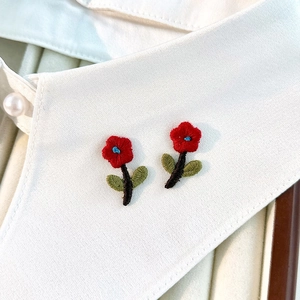 Detail of red flower embroidery patches on white collar showing fine textile texture