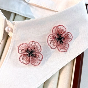 Détail de fleurs de trèfle brodées roses sur col blanc avec bouton de perle nacré