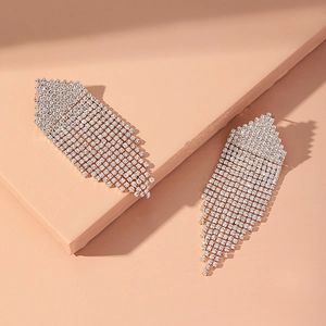 Detailed view of silver crystal tassel earrings with sparkling rhinestones on beige surface