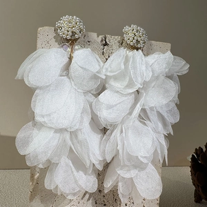 Vue détaillée de boucles d'oreilles à pompons en tissu blanc et perles sur socle