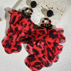 Detailed close-up of red and black leopard print fabric flower earrings on white stone