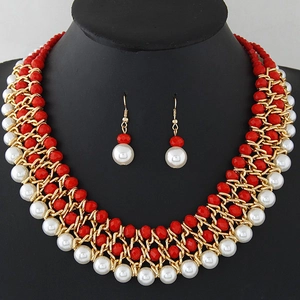 Dettaglio di un set gioielli boho intrecciato con perle rosse, bianche e metallo dorato