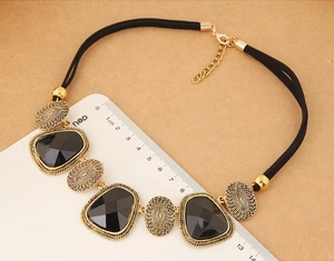 Vue détaillée d'un collier géométrique doré avec des pierres noires à côté d'une règle graduée