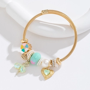 Gold twisted rope bangle with pearl, heart crystal, and floral charms on a white stand