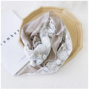 Detail of light brown linen triangle scarf featuring elegant wide white floral lace trim