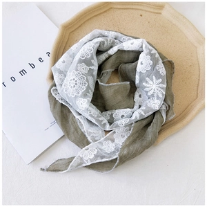 Detail of olive green fabric scarf with delicate white floral lace embroidery and soft texture