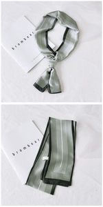 Macro view of silky narrow scarf in grey-green with dark green borders and geometric lines
