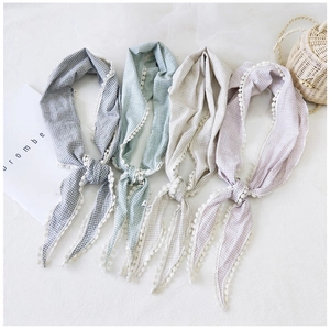 Detail of four pastel checkered scarves with white pom-pom lace edges on white fabric