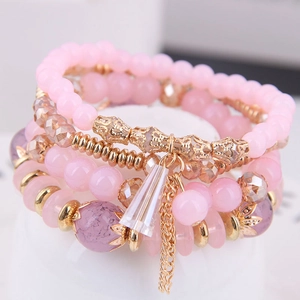 Pulsera bohemia de capas con cristales rosas y borla dorada sobre un soporte blanco