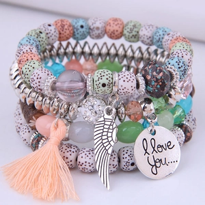 Macro detail of multilayer beaded bracelet with feather charm, tassel and heart engraving