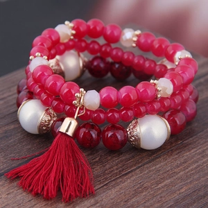 Bohemian multilayer beaded bracelet with red tassels and pearls on a wooden surface