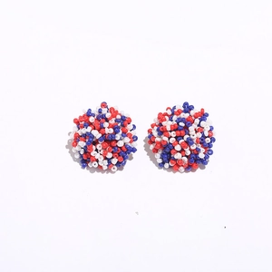 Detailed close-up of handmade bohemian beaded stud earrings in red, white and blue patterns