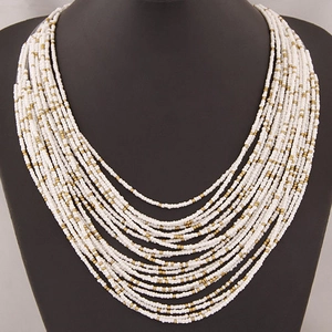 Bohemian multi-layer white seed bead necklace with gold accents on a black display stand