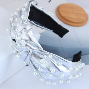 Silver metallic wide knot headband with white faux pearls on a minimalist white display