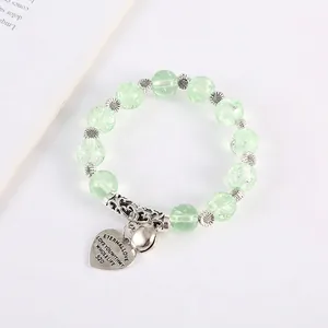 Detail of light green beaded bracelet with silver flower charms and heart tag