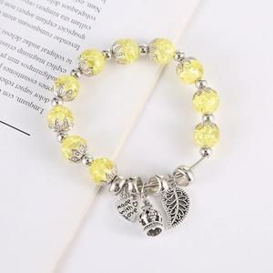 Dettaglio del bracciale di perle di vetro giallo con ciondoli a cuore corona e foglia