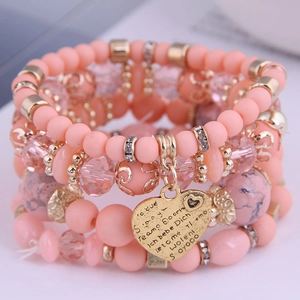 Macro detail of multi-layer beaded bracelet with engraved heart charm and crystals
