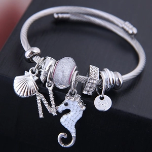 Silver woven bracelet with enamel seahorse, shell, and crystal charms on a jewelry box