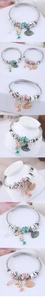 Detail of ocean-themed steel wire bracelet featuring mermaid, shell, and enamel flower charms