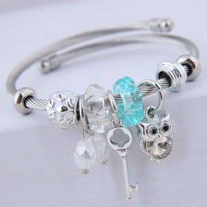 Silver twisted wire charm bracelet with owl pendant and blue faceted beads on white stand