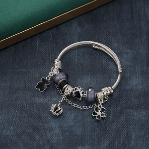 Adjustable charm bracelet with black bear, crown, and purple beads on blue background