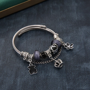 Silver bead charm bracelet with bear, crown and purple crystals on blue fabric