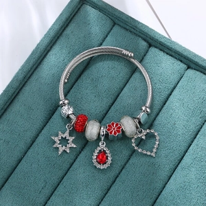 DIY Perlenarmband mit rotem Kristalltropfen und Herzanhängern auf blaugrünem Samt