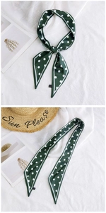 Detail of dark green polka dot silk scarf with brand logo on soft cotton background