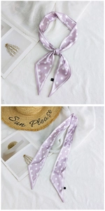 Detail of lavender polka dot skinny silk scarf tied in a bow on a white textured backdrop