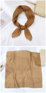 Detail of a brown plaid linen scarf tied on a straw bag and laid flat on a white surface