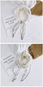 Detail of white mesh scarf with delicate black wavy edges displayed on a rustic background