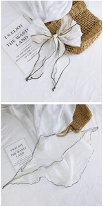 Detail of white semi-transparent mesh scarf with black wavy edges and bow styling