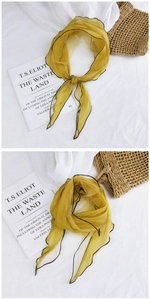 Close-up of ginger yellow sheer scarf with black contrast hem on white textured fabric