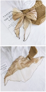 Detail of champagne organza scarf with black wavy edges tied in an elegant bow