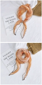 Detail of soft apricot mesh scarf with black contrast hem on woven hat and book background