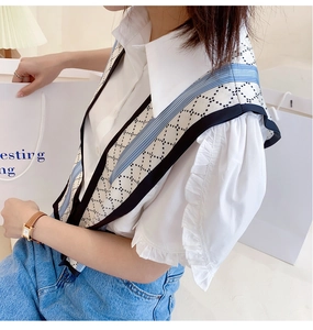 Detail of a layered blue geometric silk scarf styled over a white blouse with ruffles