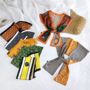 Flat lay of colorful patterned narrow silk scarves on white linen with a straw hat