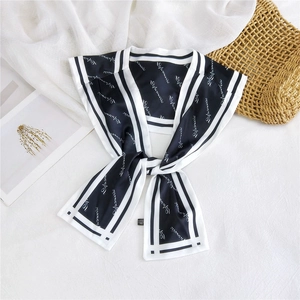 Detail of a black silk scarf with white lettering and a knot tied on soft fabric